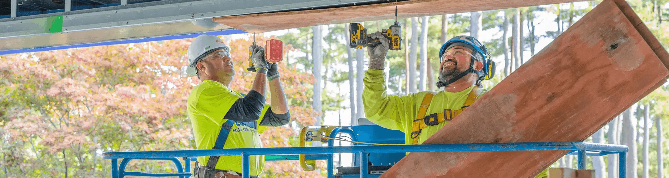 Two men in safety gear screwing into wood