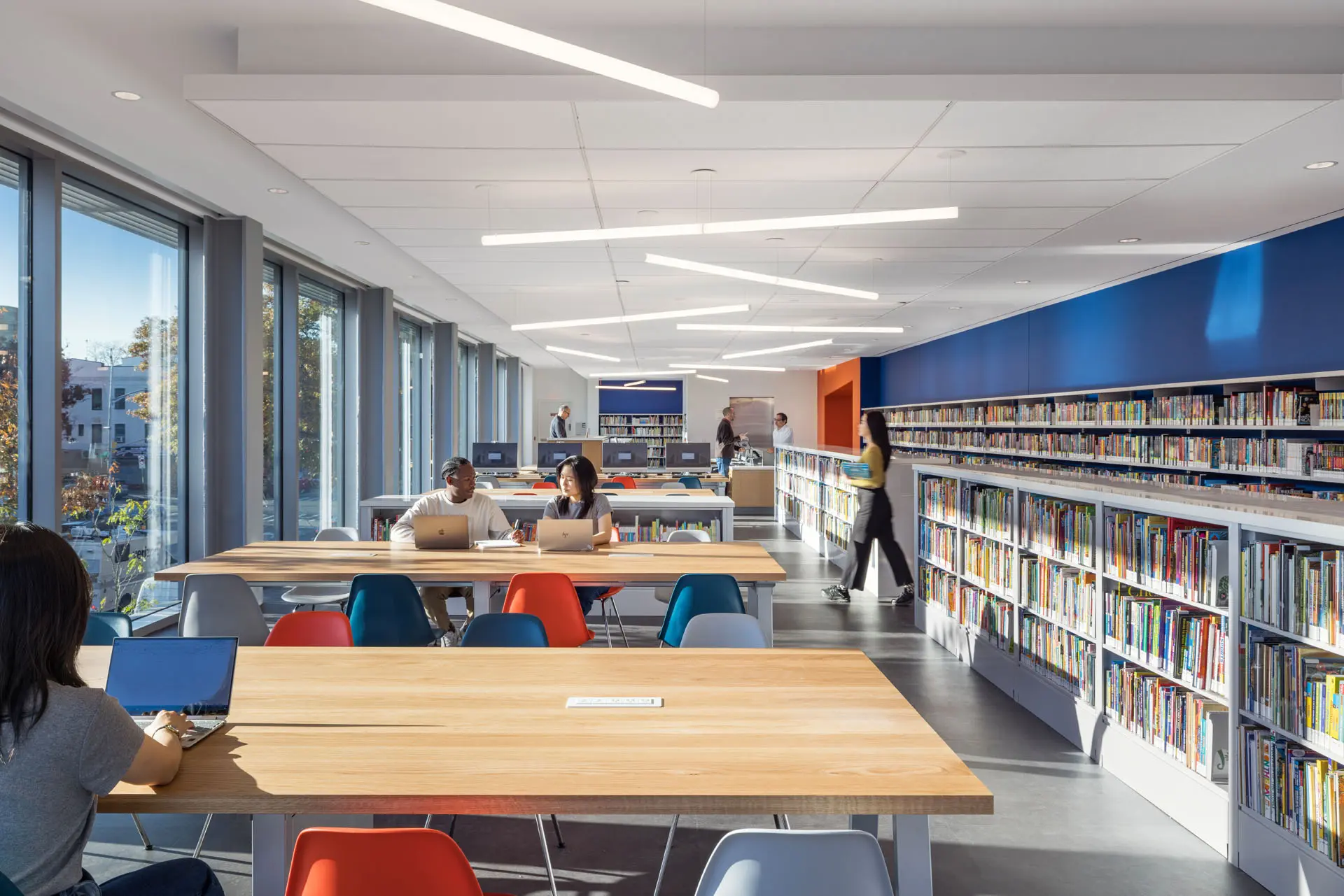 Rendering of library with large windows, eight seated tables, and two rows of bookshelves