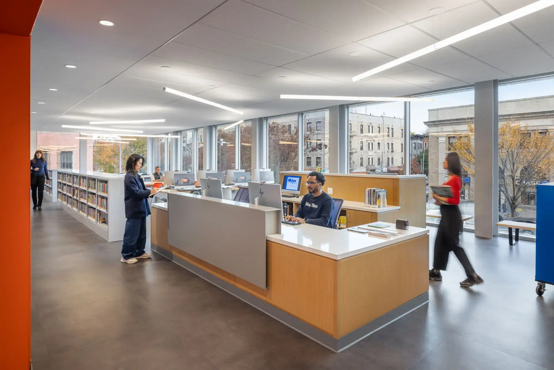 Rendering of Man at computer desk with people milling about the area in front of large glass windows