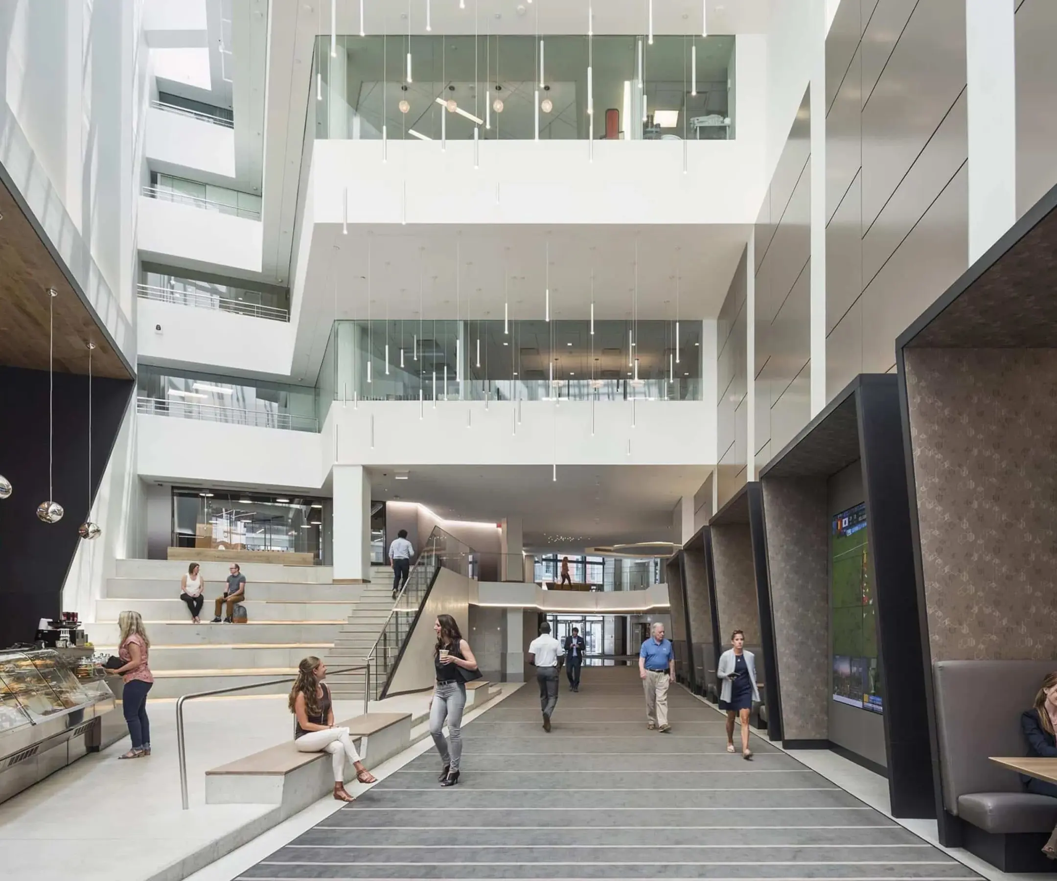 Multi-story atrium inside building with white walls, cafe, TV screen, and booths