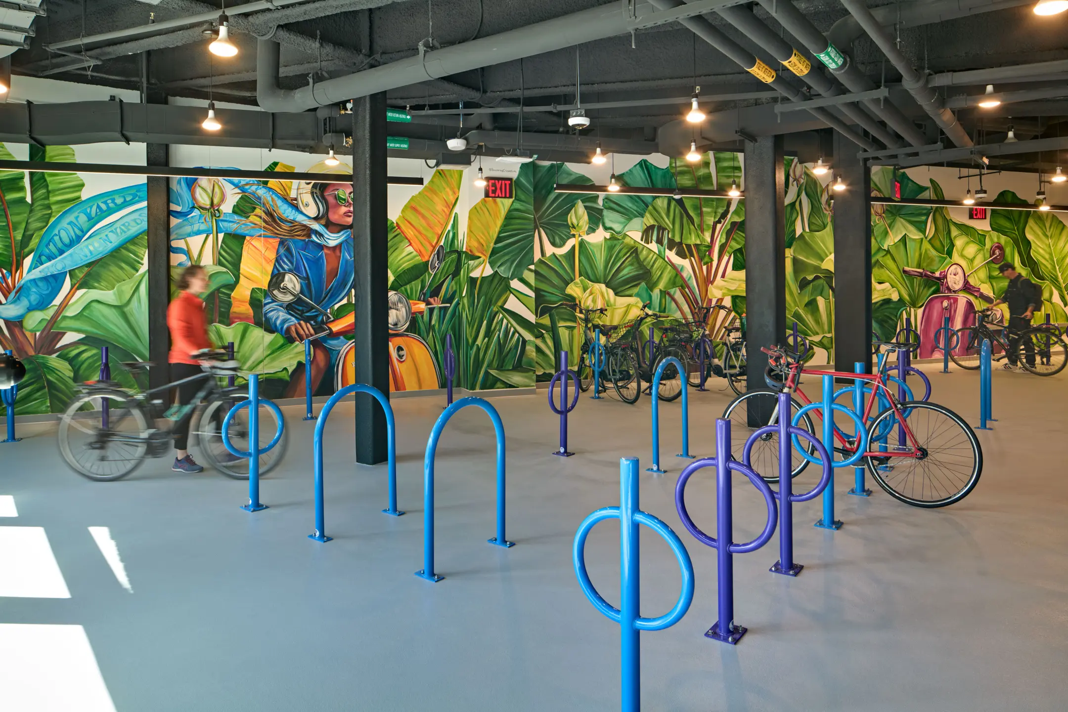 Bike racks in large room with mural of mopeds and plants