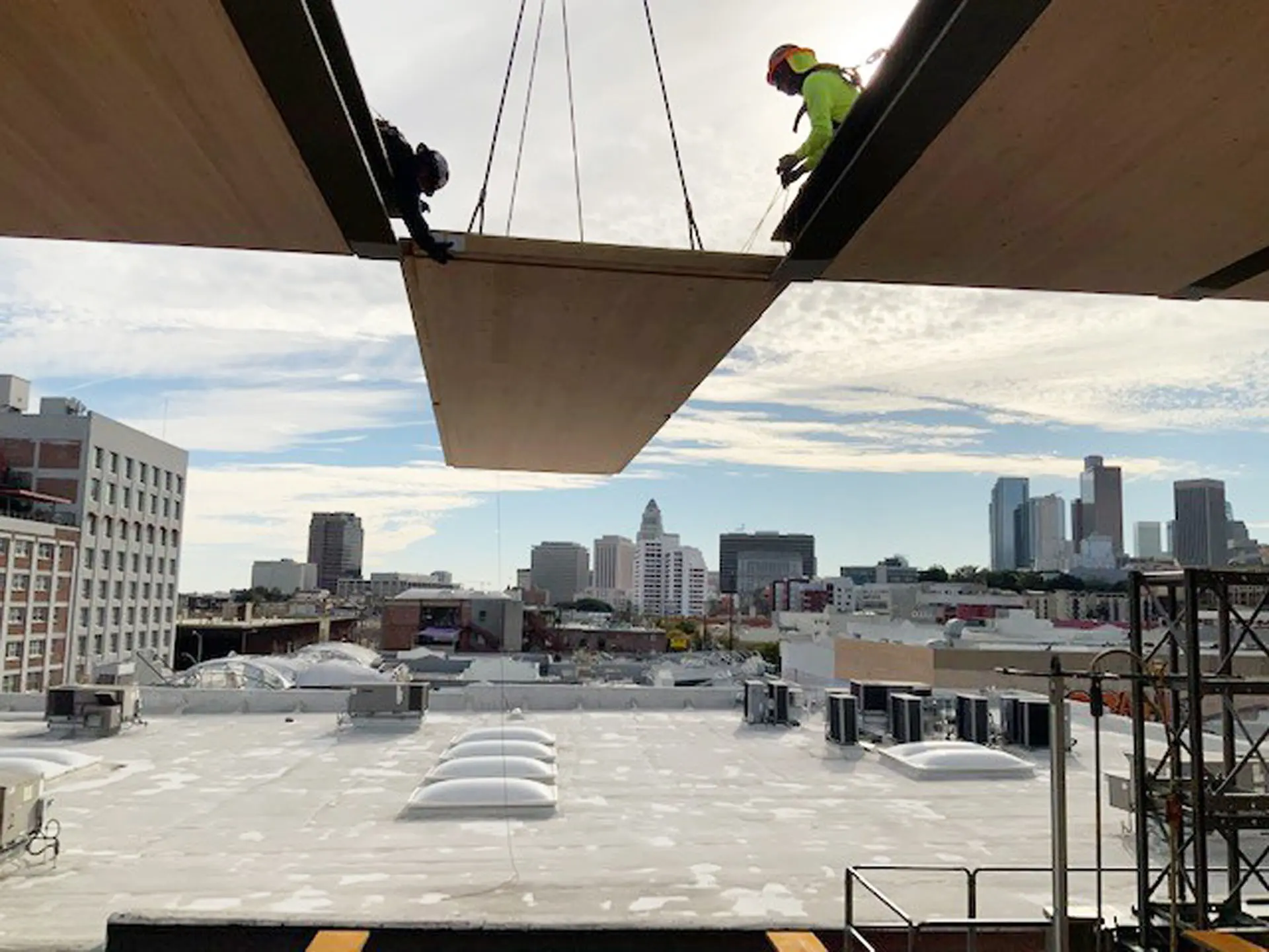 Two workers in safety gear placing wooden flooring into steel beams at the 843 North Spring Street building
