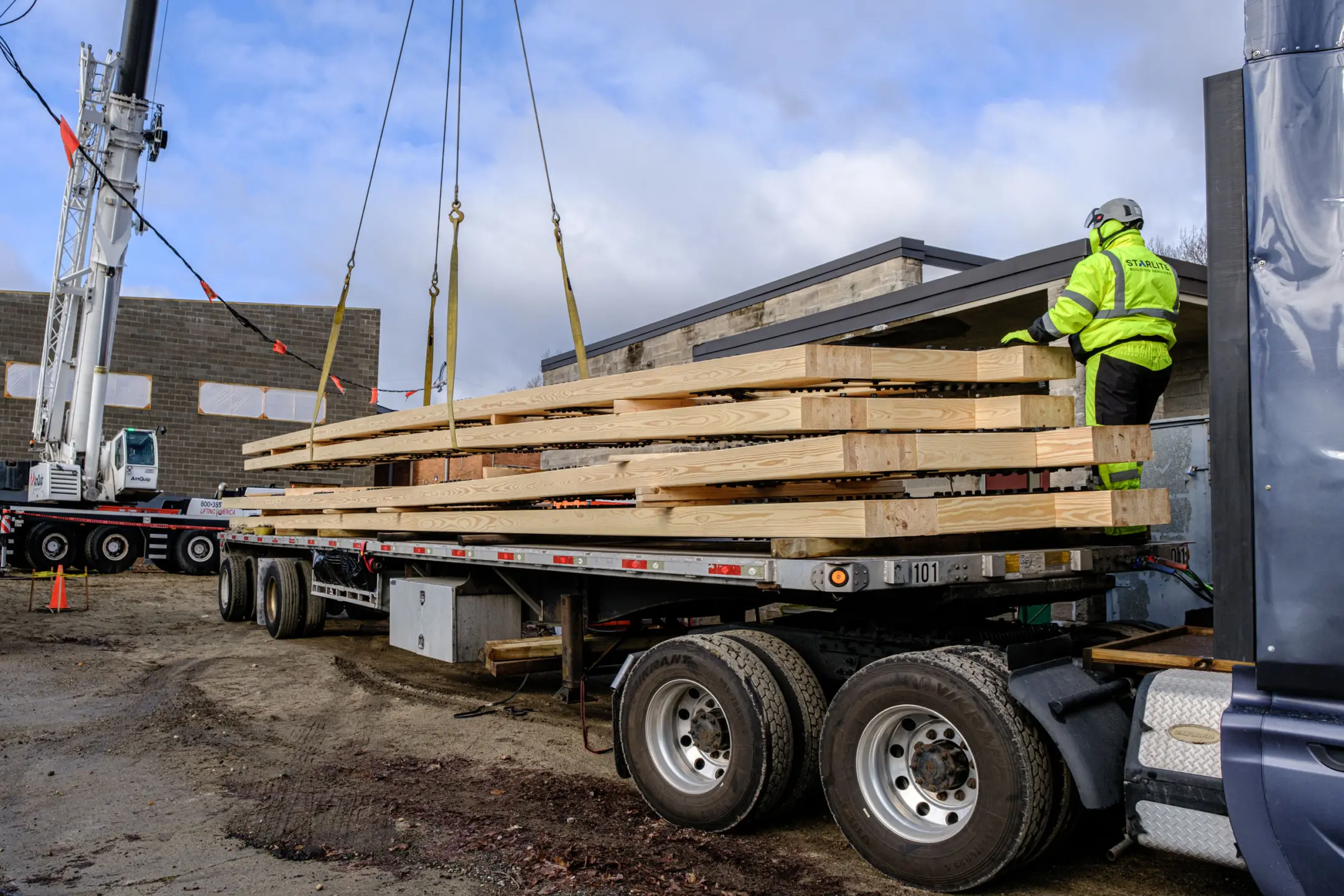 Crane lifting two timber trusses from truck with assistance from worker