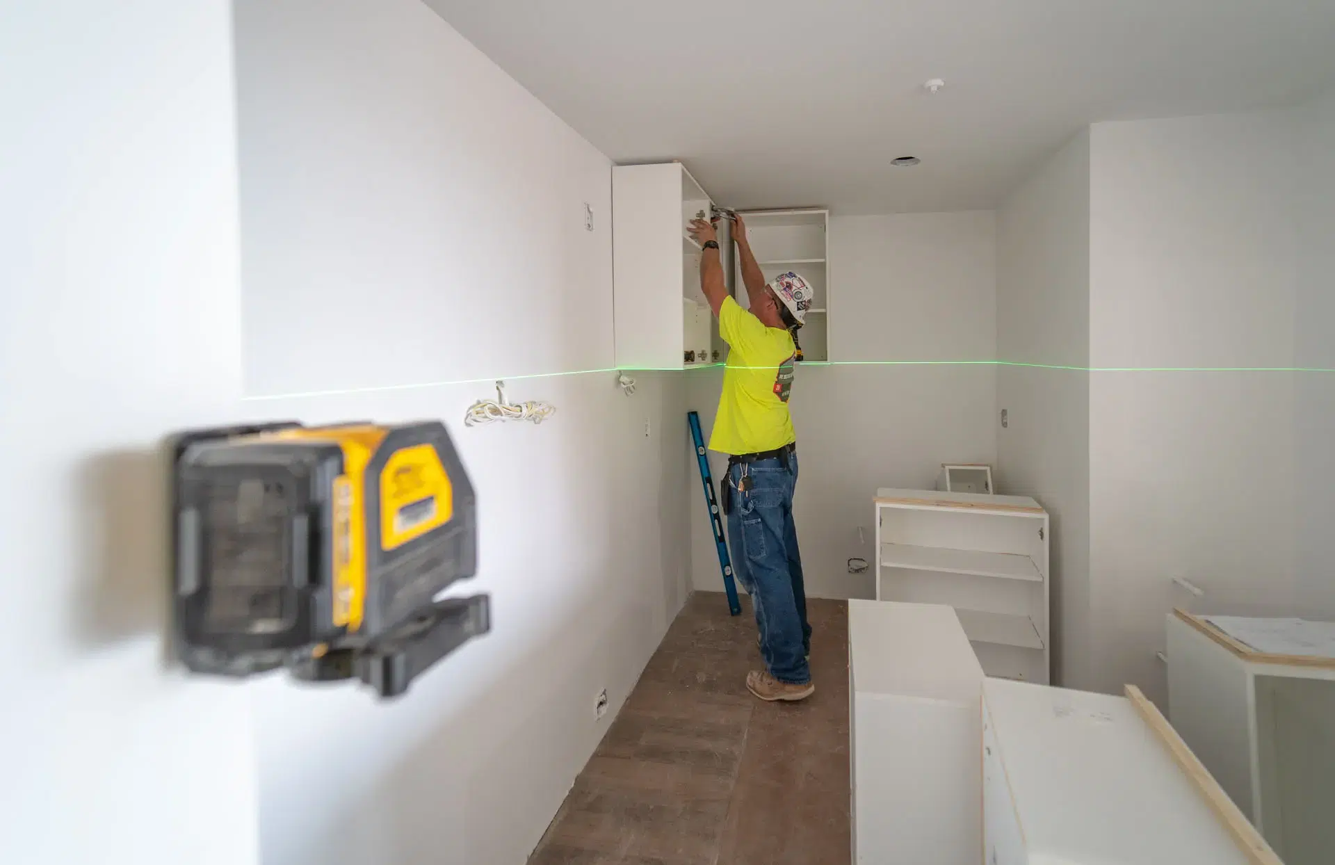 Worker installing millwork using a laser in kitchen of apartment in Harvard Soldiers Field Apartments