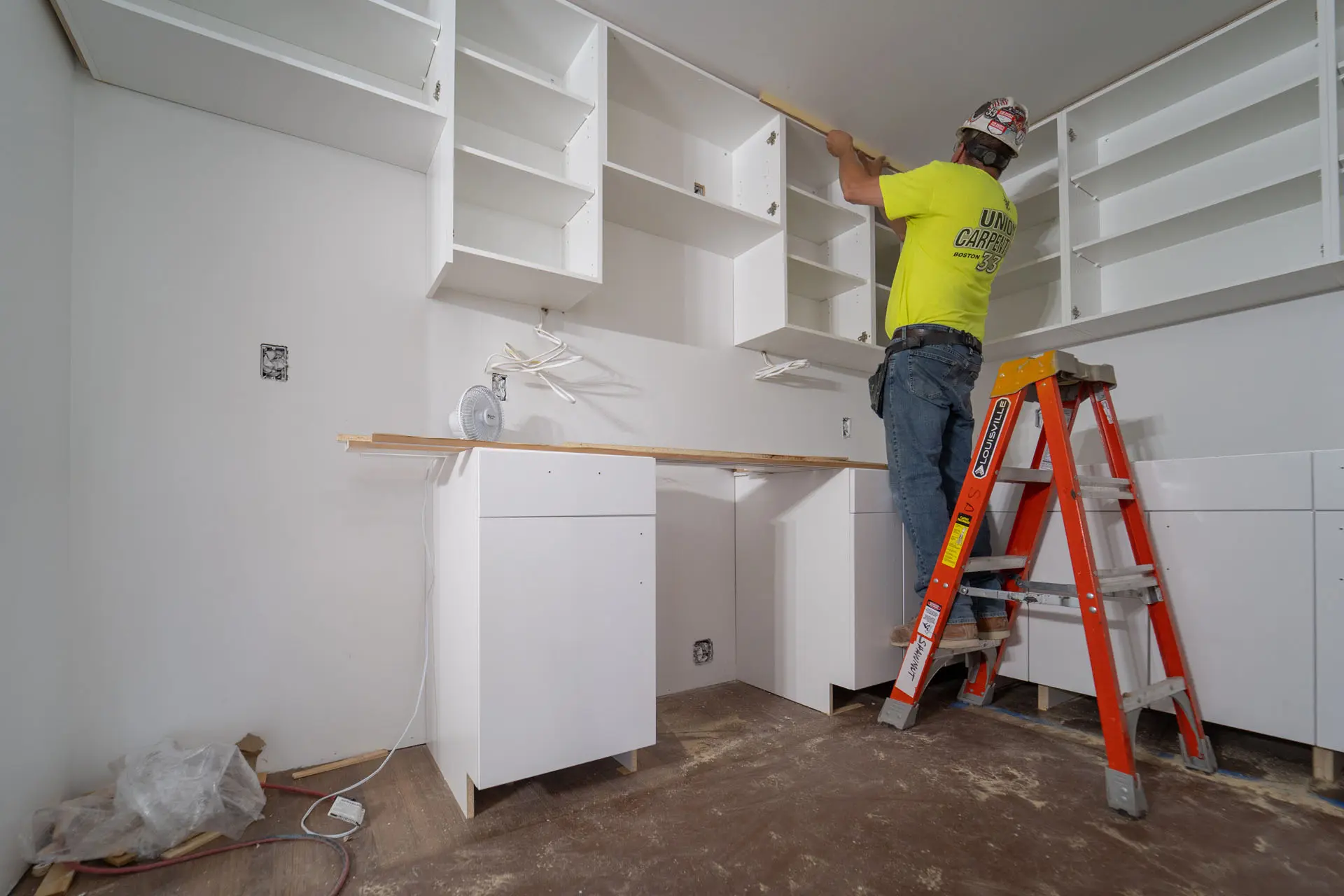 Worker on ladder installing millwork in kitchen of apartment in Harvard Soldiers Field Apartments
