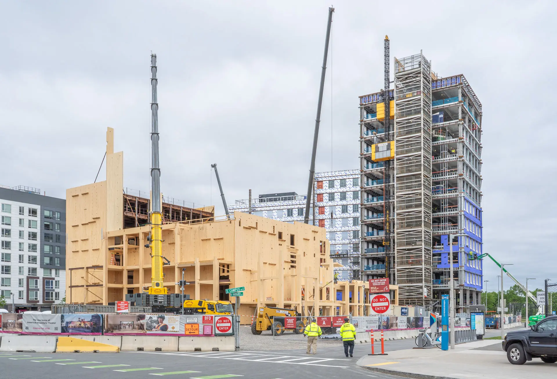 Five cranes at different locations and heights placing wooden beams, lifting workers, and placing steel at Harvard University American Repertory Theatre