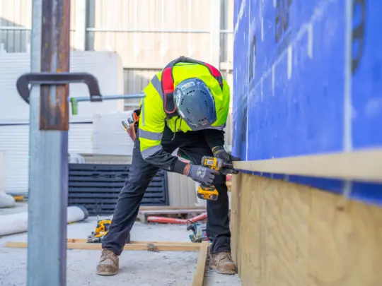Worker in safety gear crouching working on drilling
