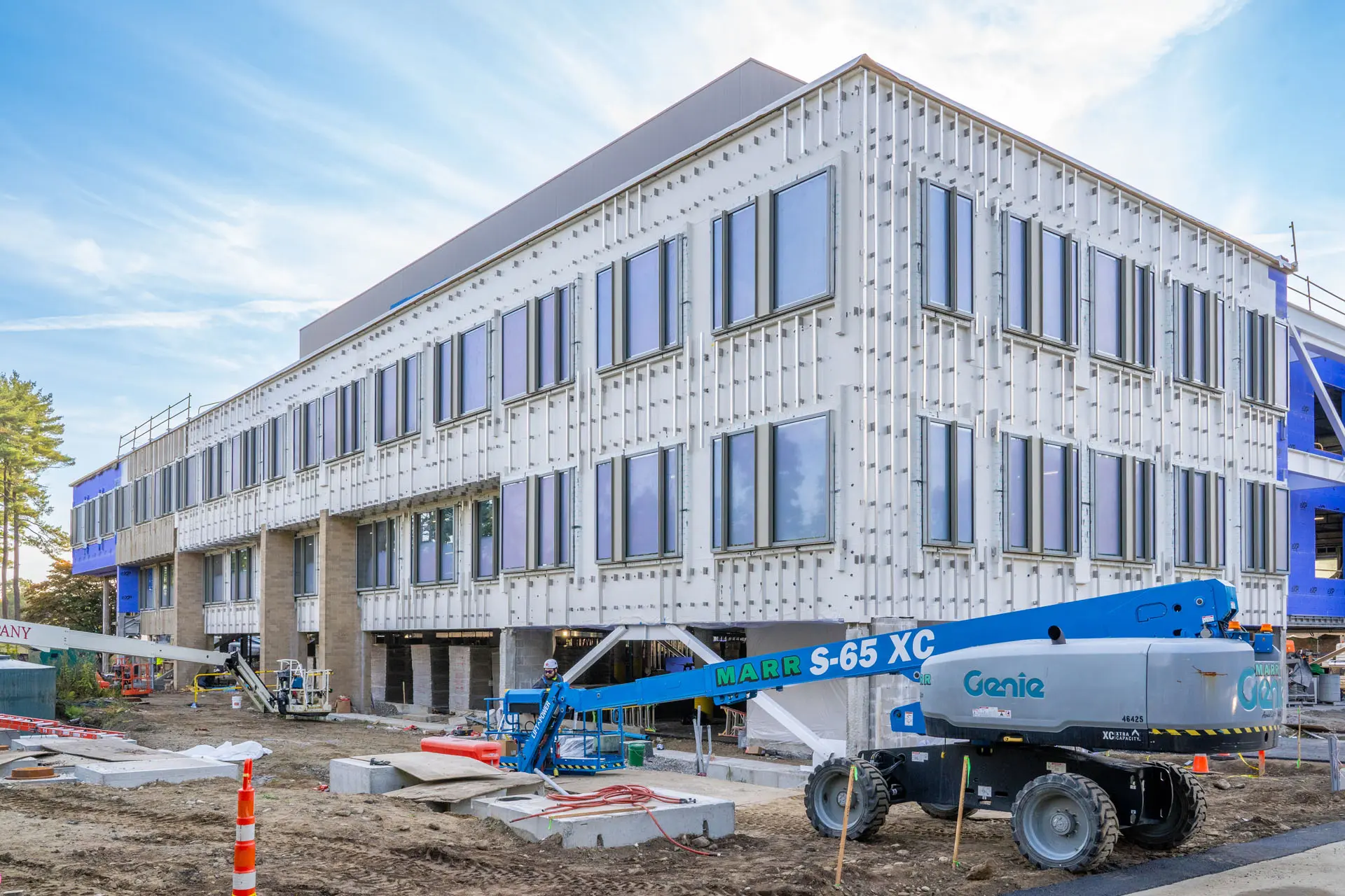Blue cherrypicker with worker in front of two story Riverside Lab building under construction