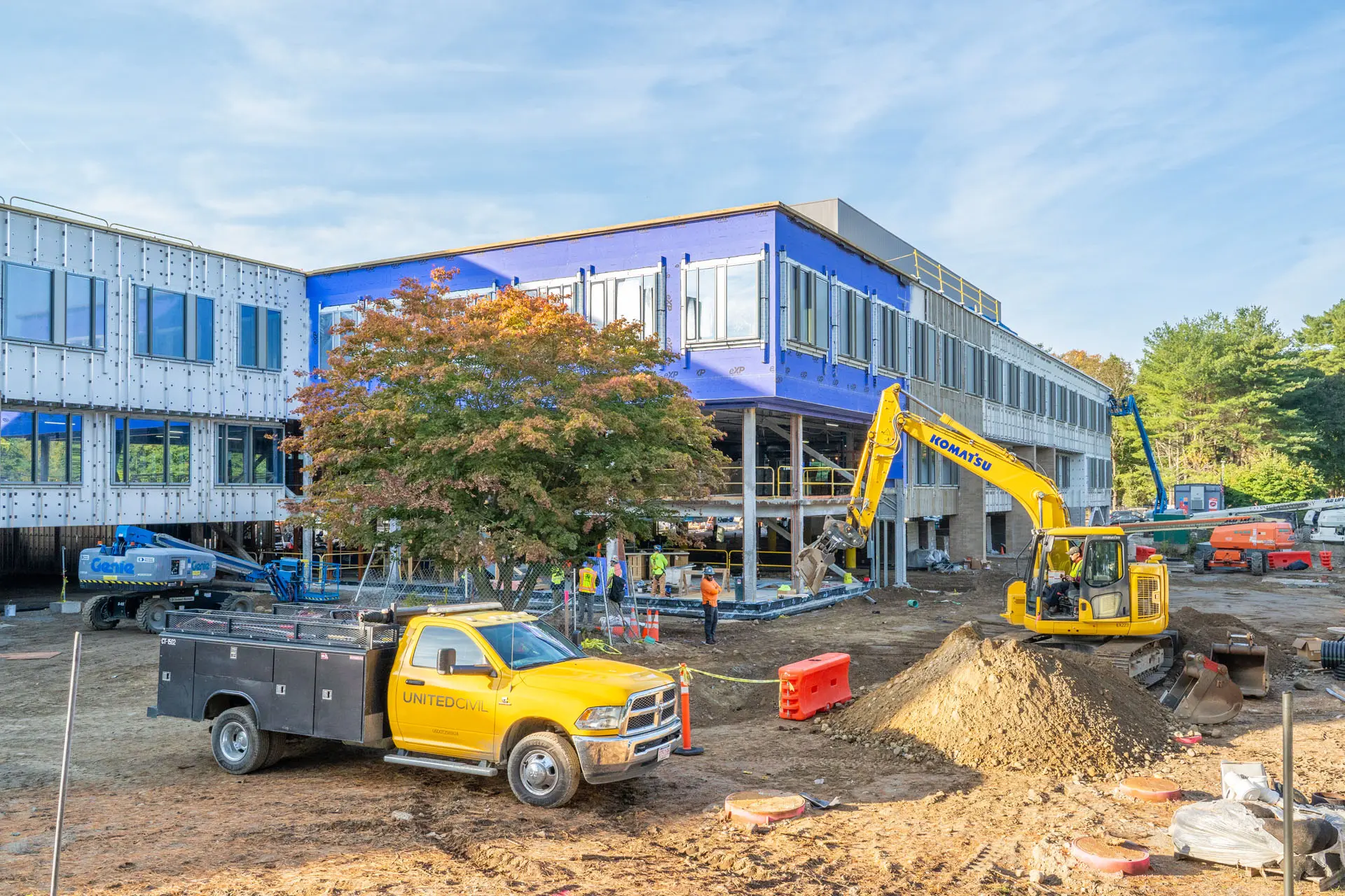 Yellow work truck and yellow backhoe in yard area in front of Riverside Labs two story building under construction
