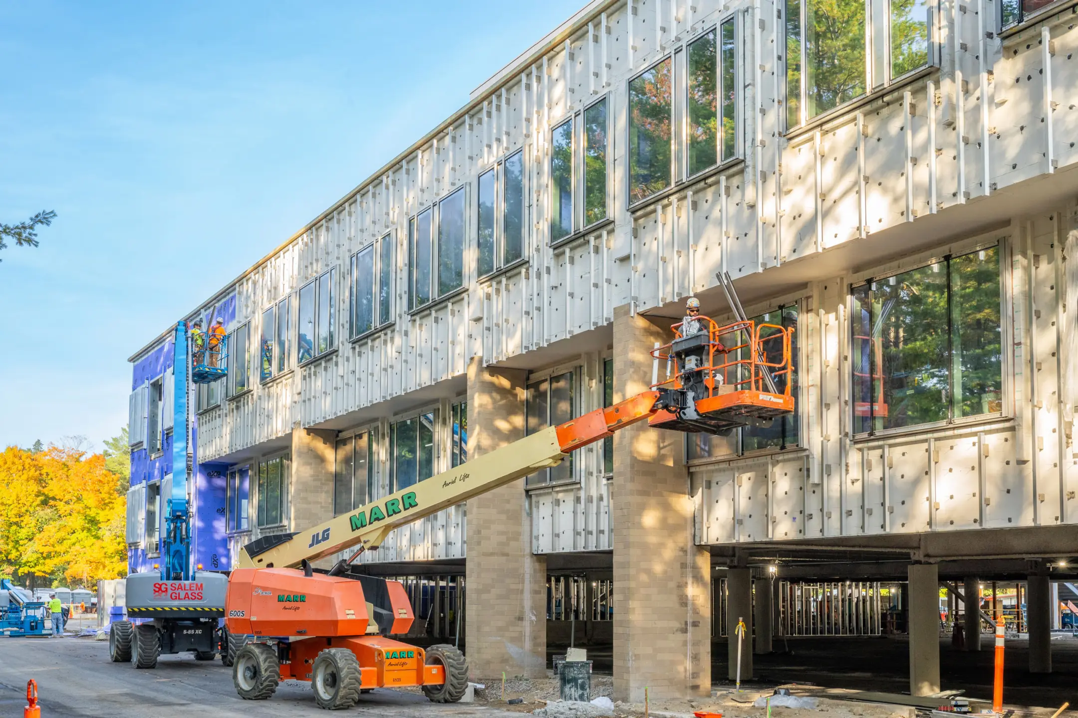 Cherrypicker lifting worker beside two story building under construction