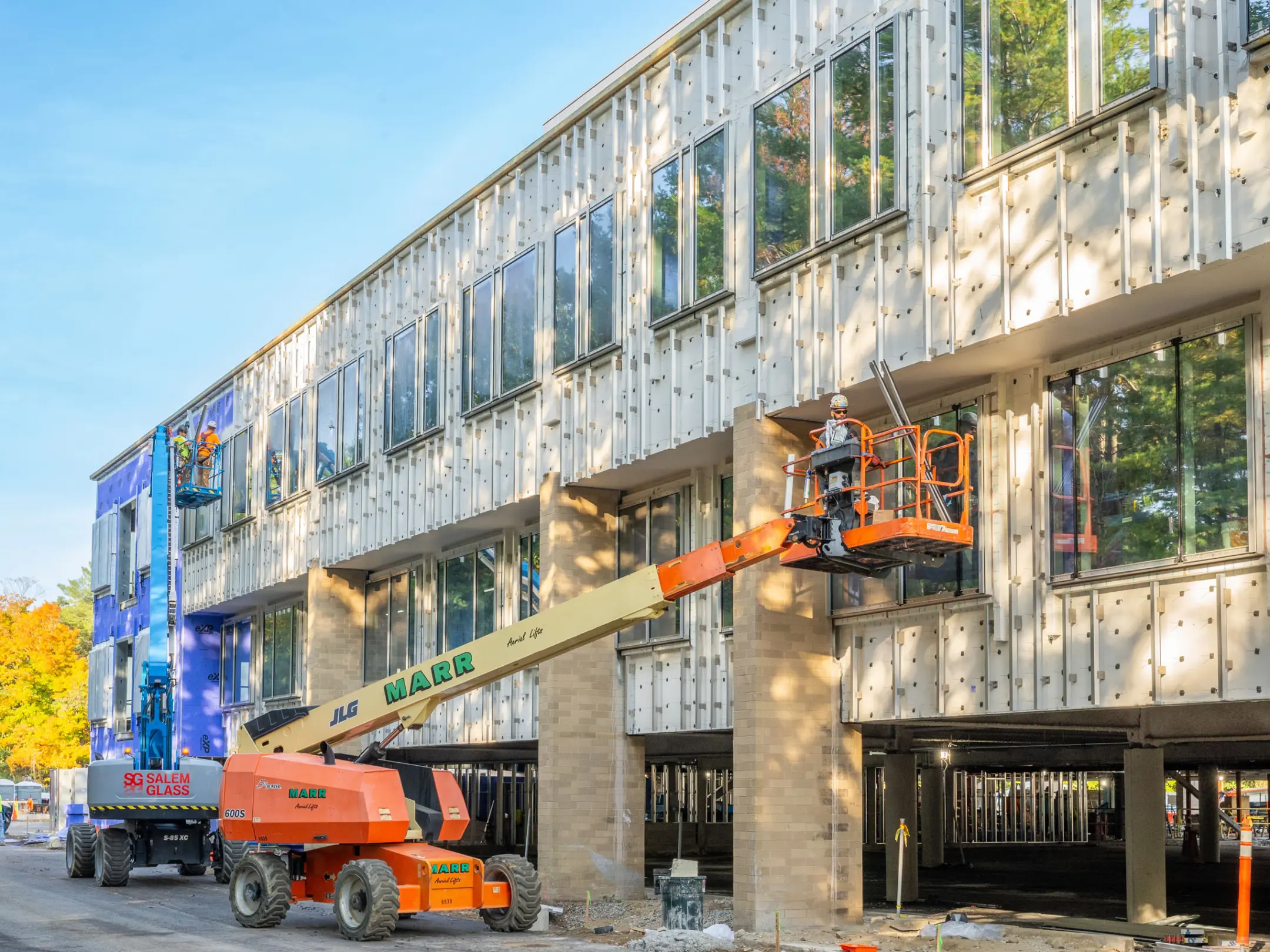 Cherrypicker lifting worker beside two story building under construction