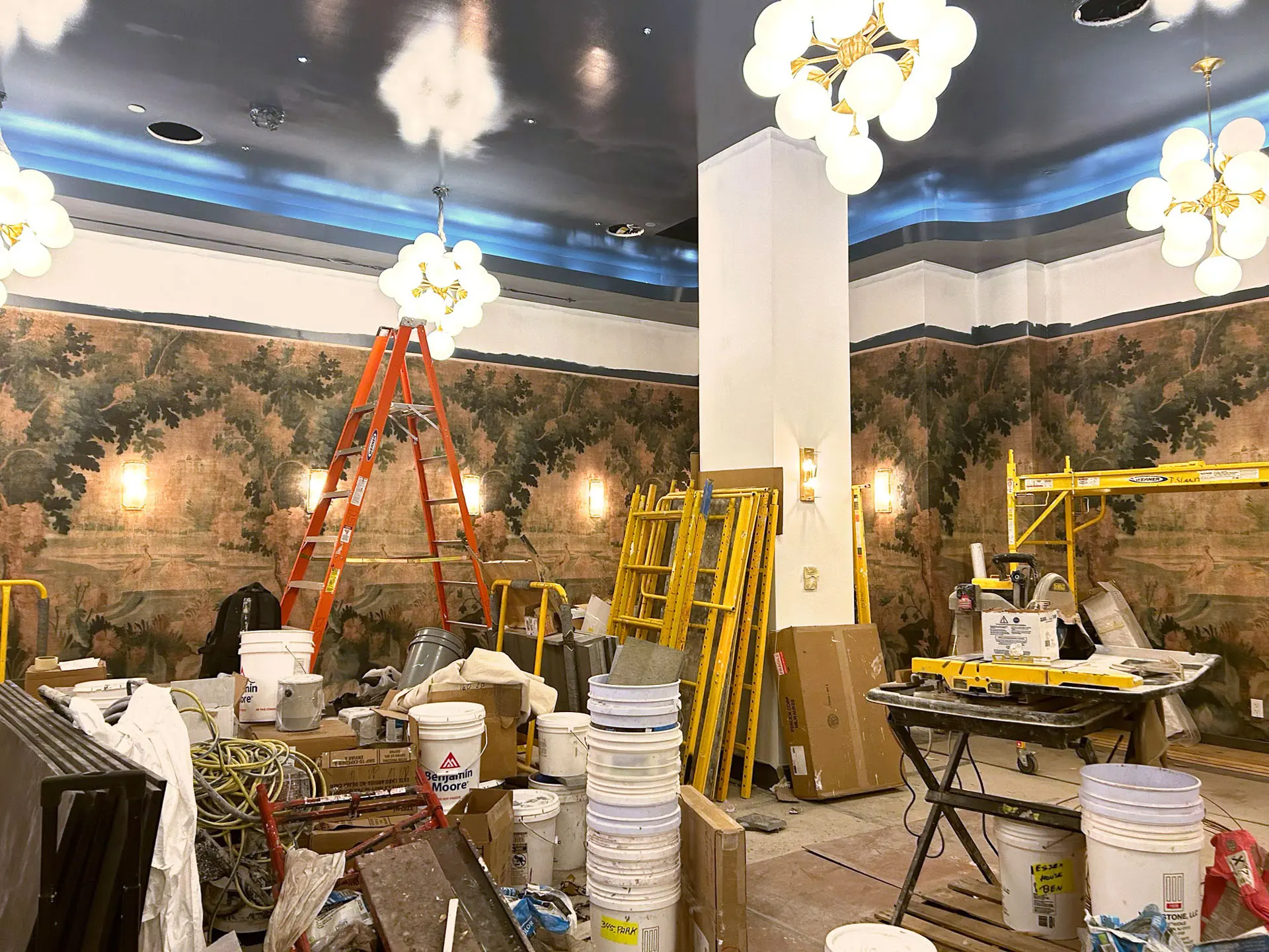 Interior progress of hotel with mural wall, globe chandeliers, and wall sconces