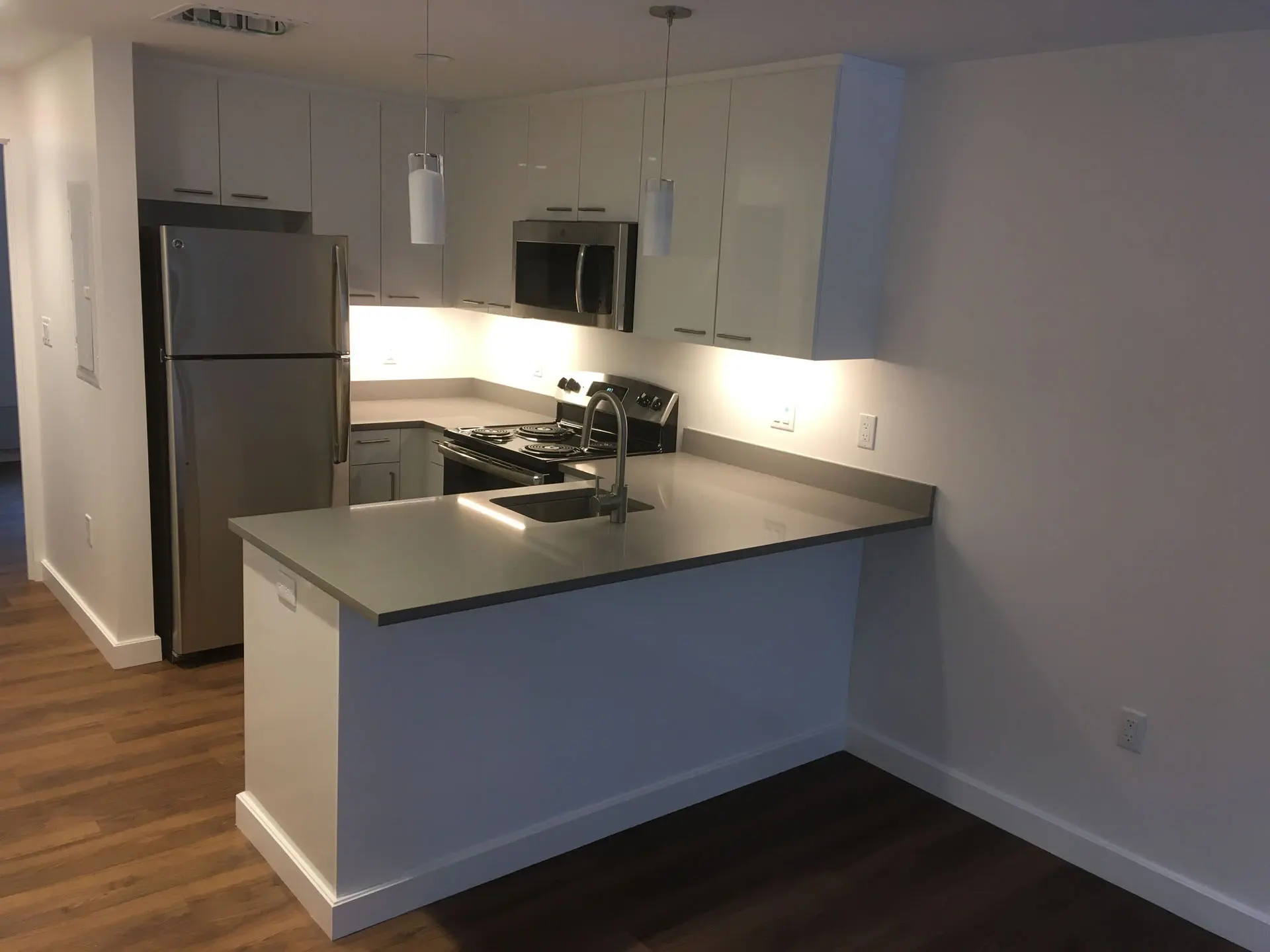 Interior of kitchen in apartment building with sink, fridge, range, and microwave, and pendant lights