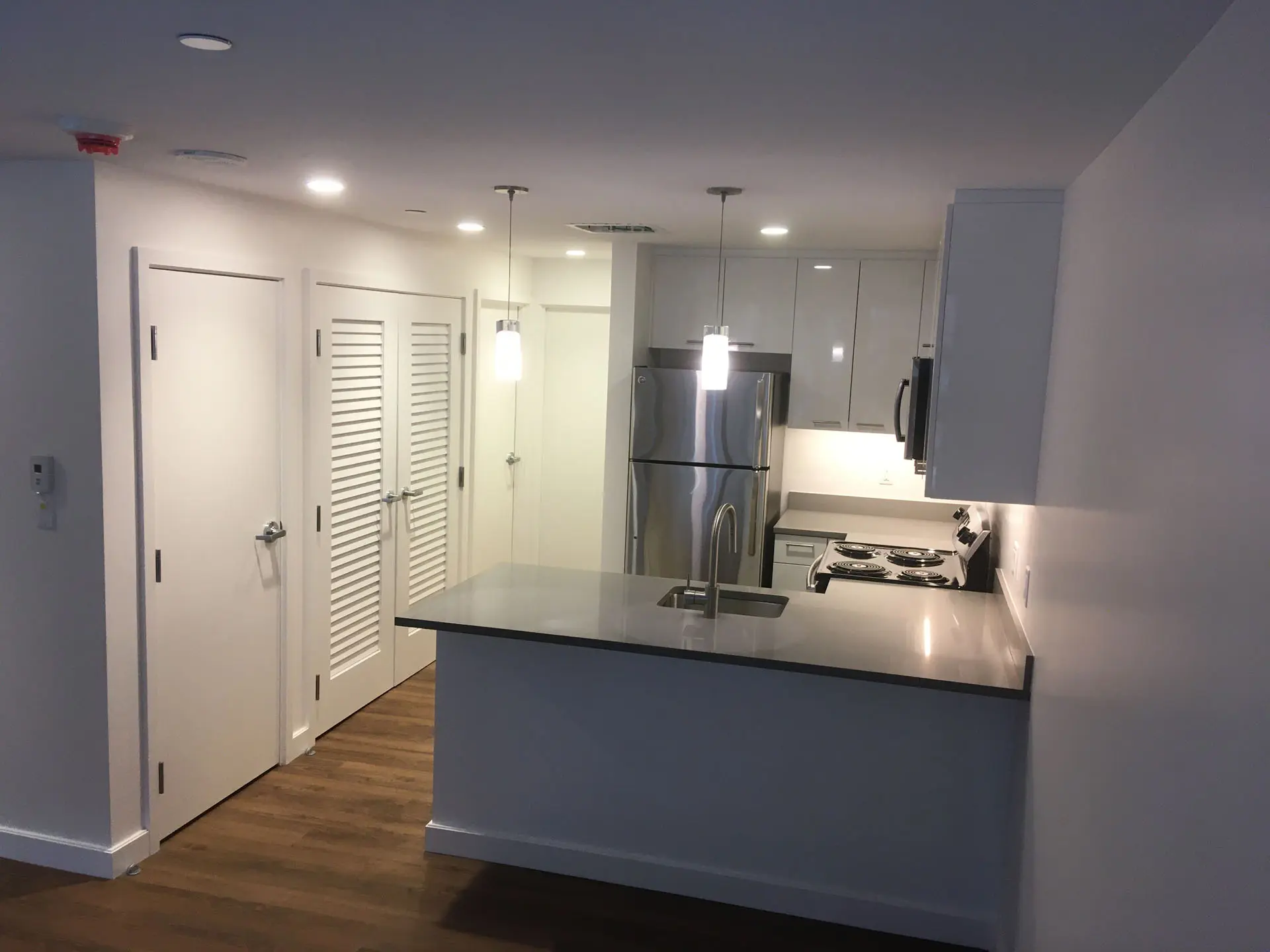 Interior of kitchen in apartment building with sink, fridge, range, and microwave, and pendant lights