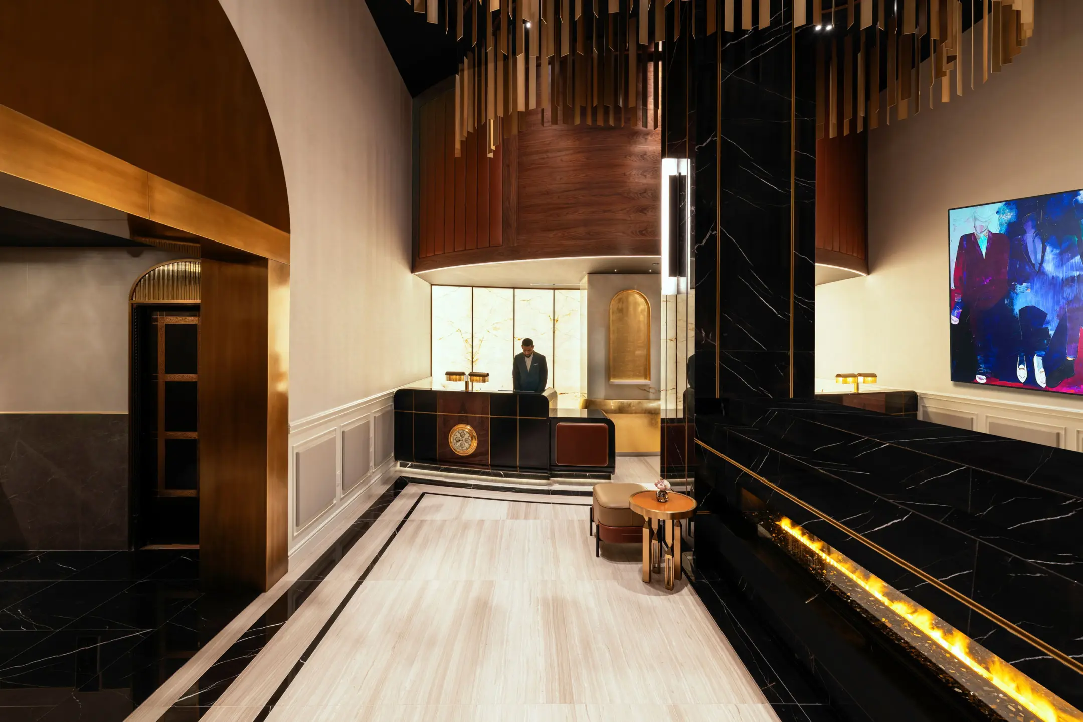 Lobby of hotel with black marble fireplace, wooden concierge desk with concierge behind, and entryway to hall