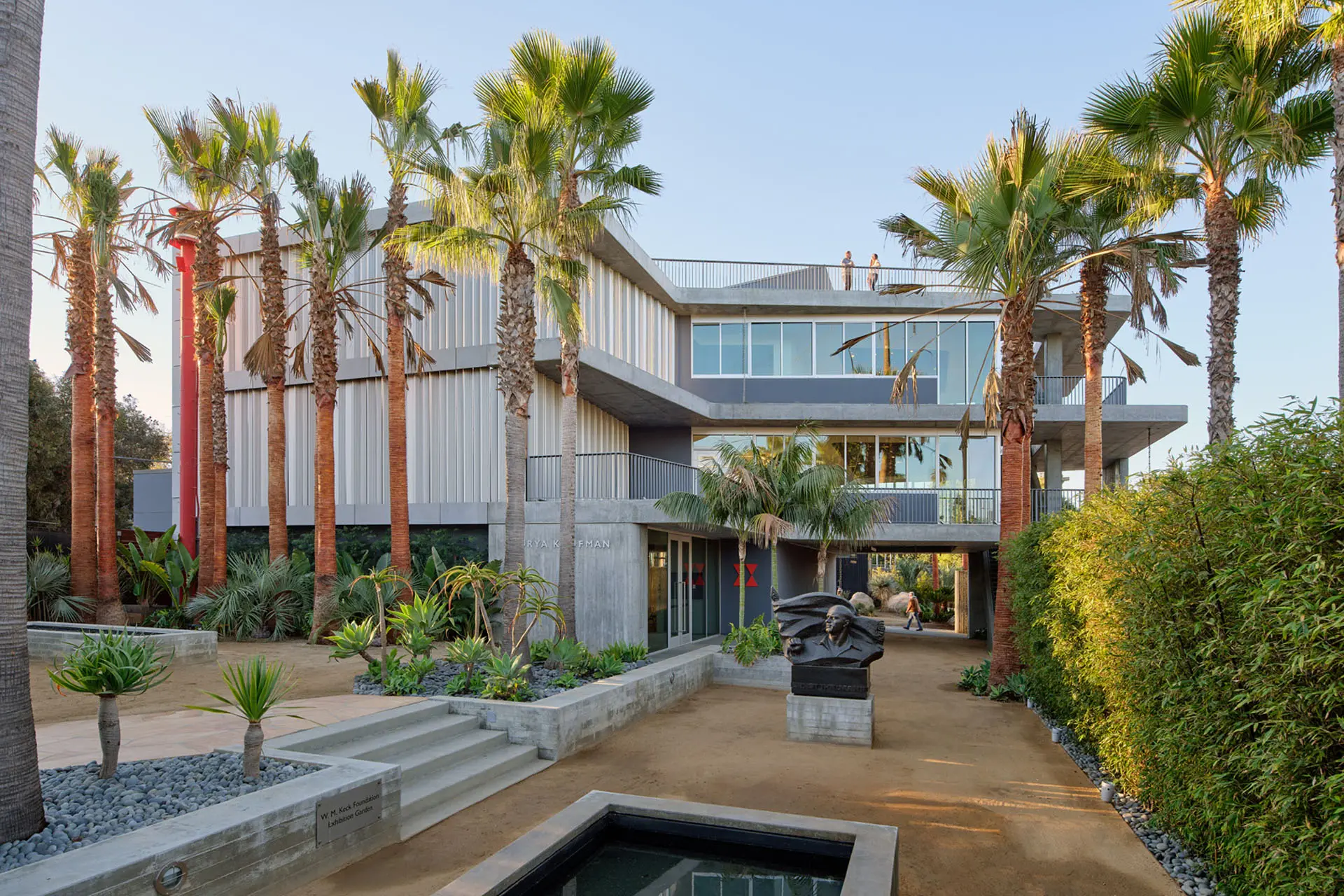 Three story concrete and glass building with palm trees and garden area