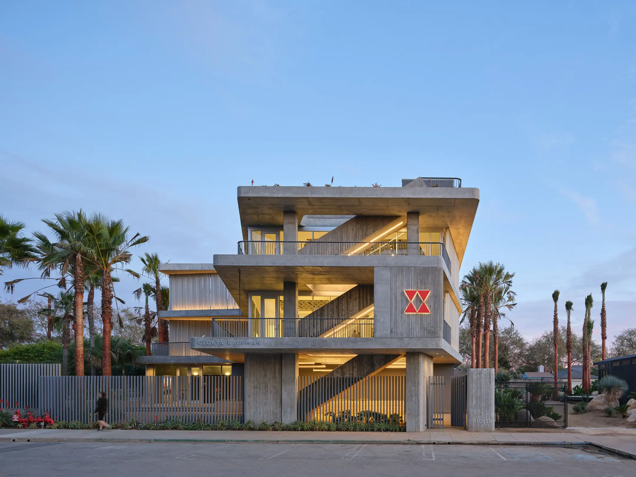 View from road of three story concrete and glass building with palm trees out front at night
