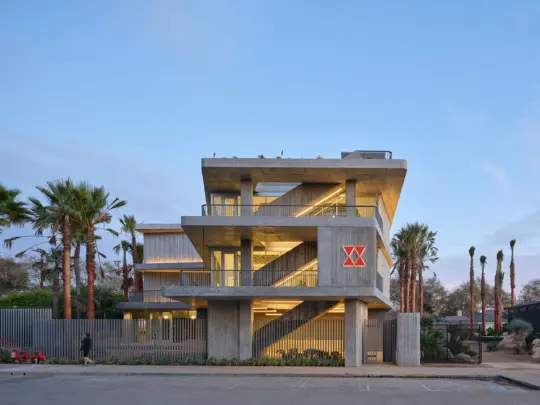 View from road of three story concrete and glass building with palm trees out front at night