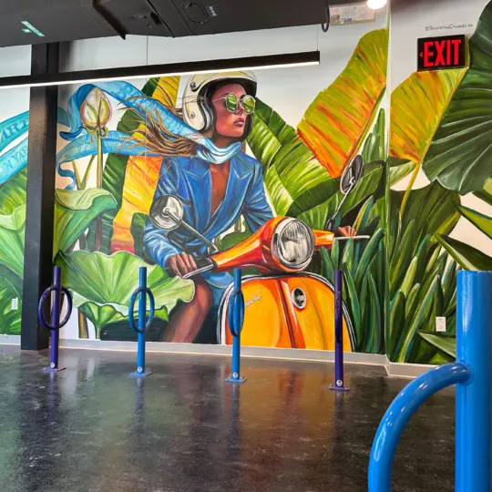 Room with bikeracks and mural of woman on mope and plants