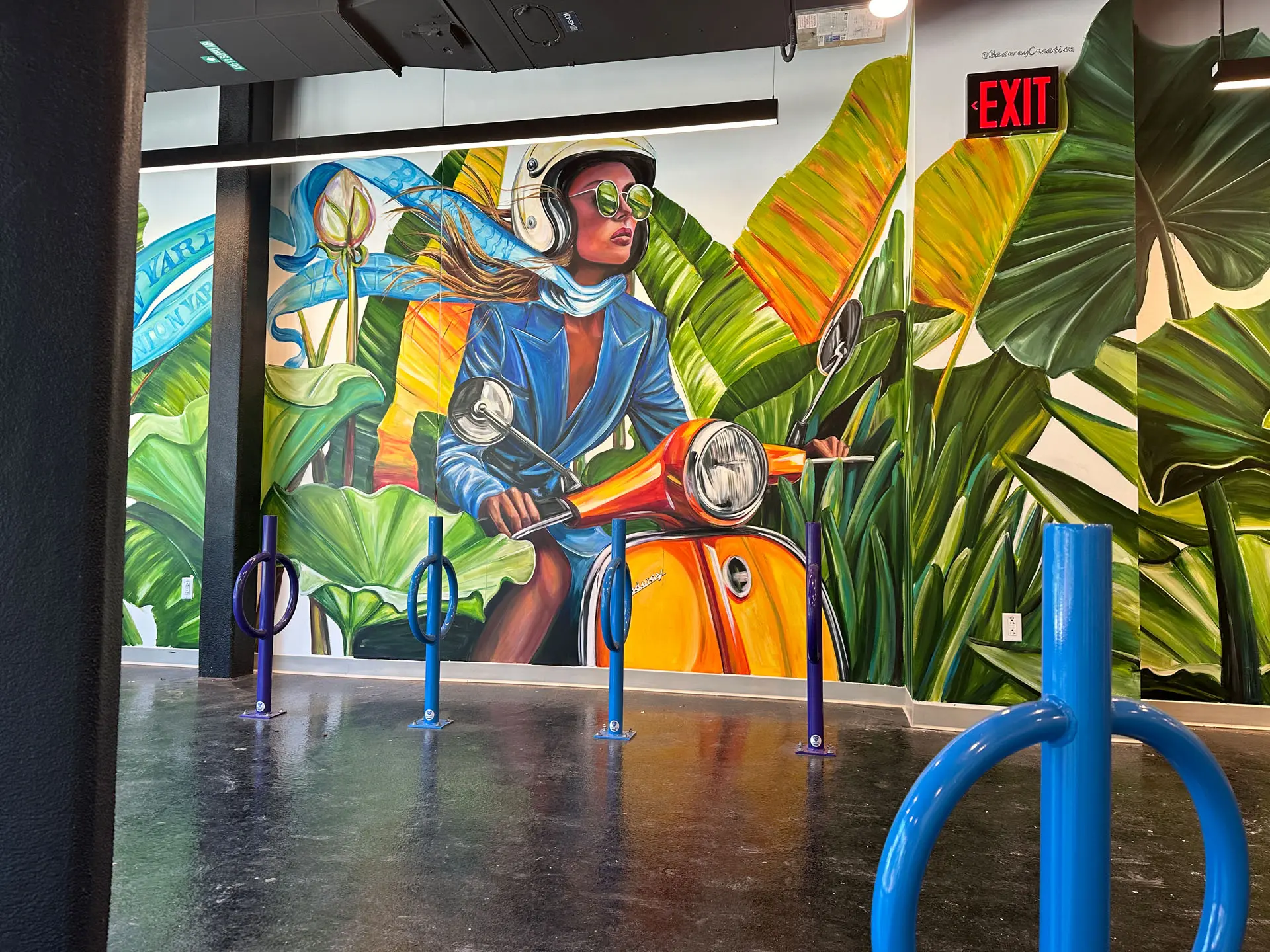 Room with bikeracks and mural of woman on mope and plants