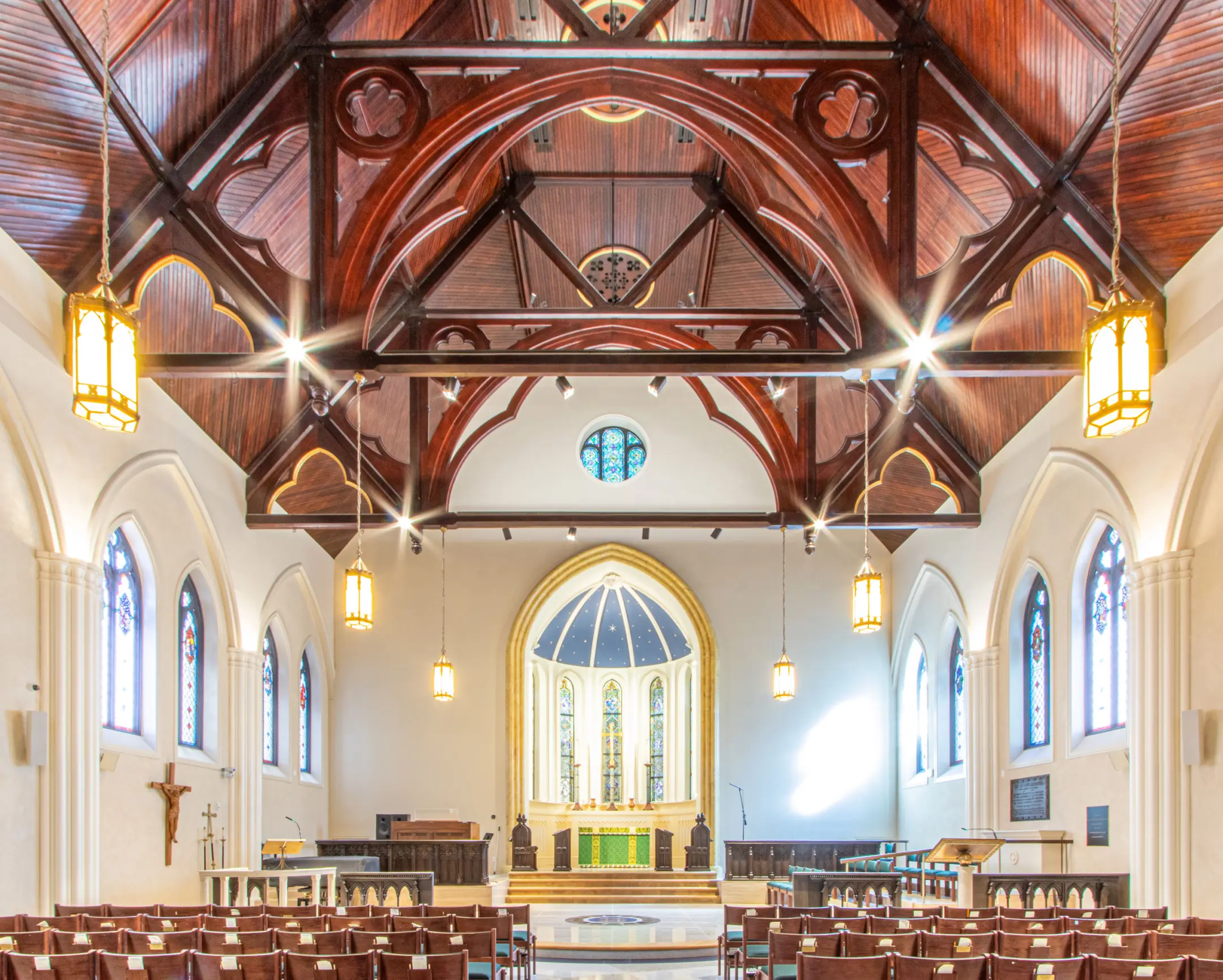 Interior image of wooden ceiling of church sanctuary with tabernacle, stained glass windows, and pendant lights