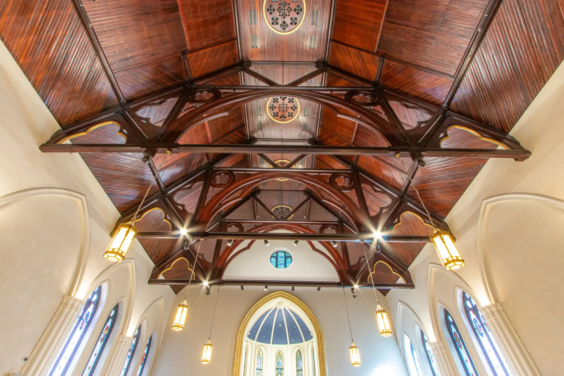 Interior image of wooden ceiling of church sanctuary with stained glass windows, and pendant lights