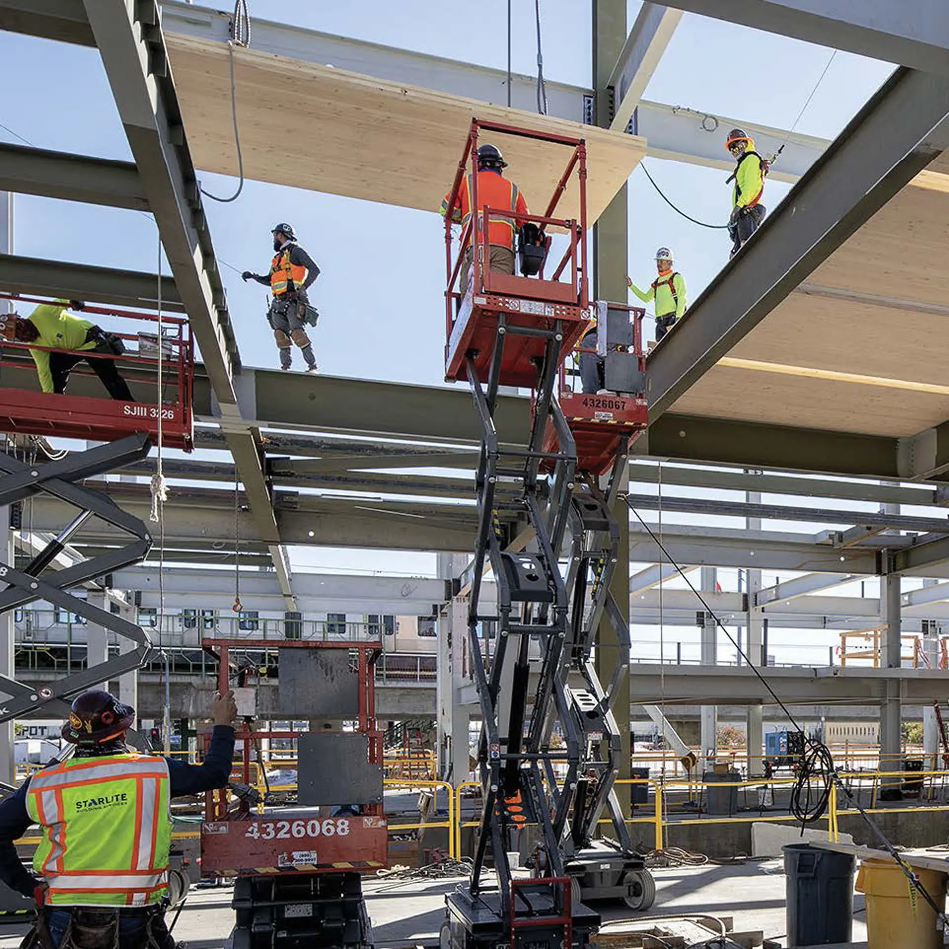 Six construction workers in safety gear working around scissor lift to place wooden flooring on steel beams at the 843 North Spring Street building