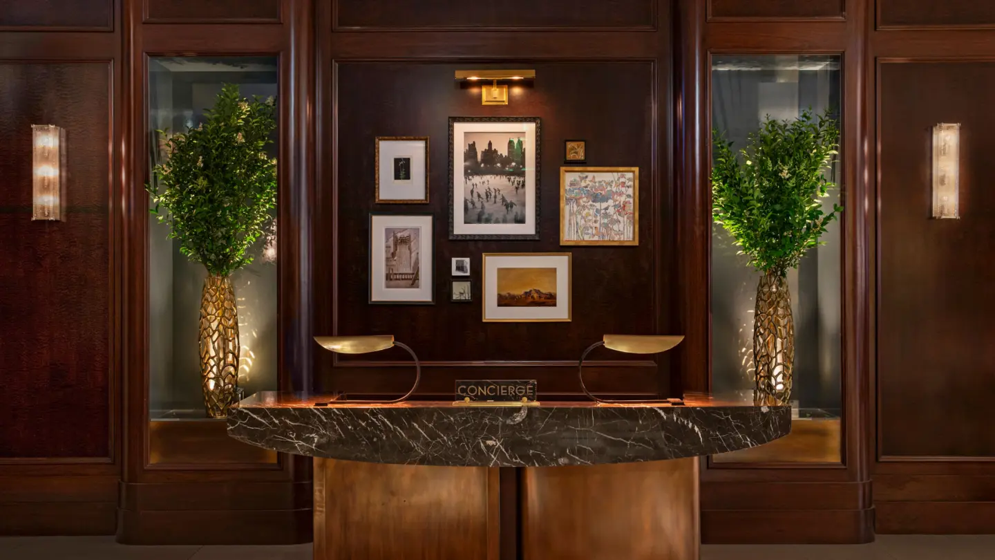 Concierge desk with dark wooden millwork behind with large greenery in vases