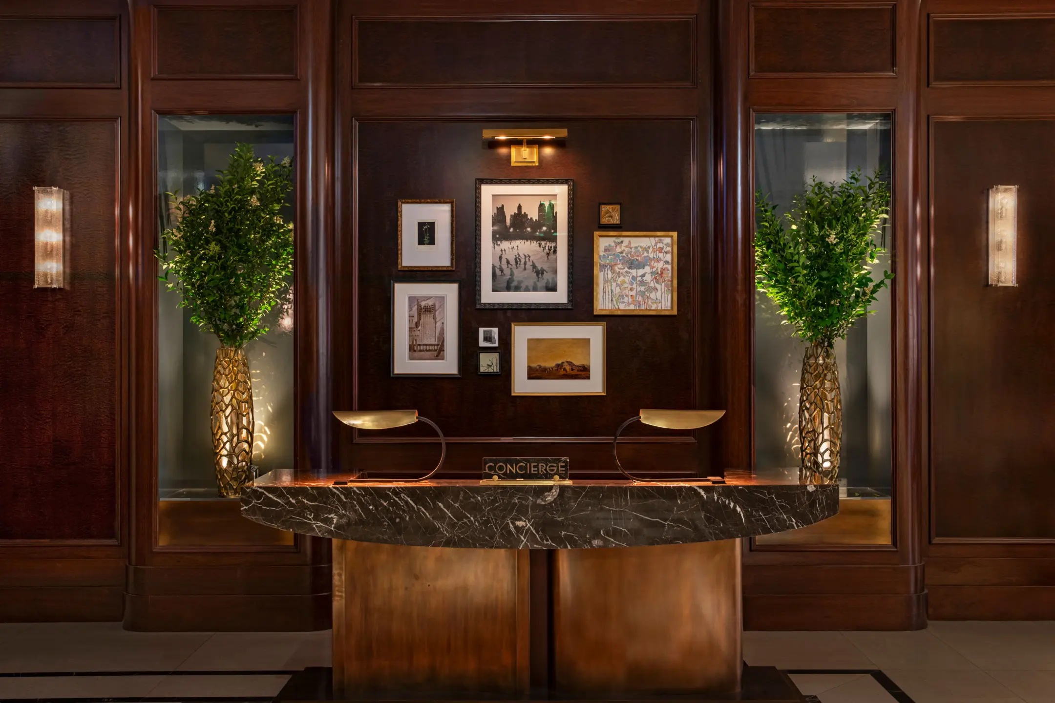 Concierge desk with dark wooden millwork behind with large greenery in vases