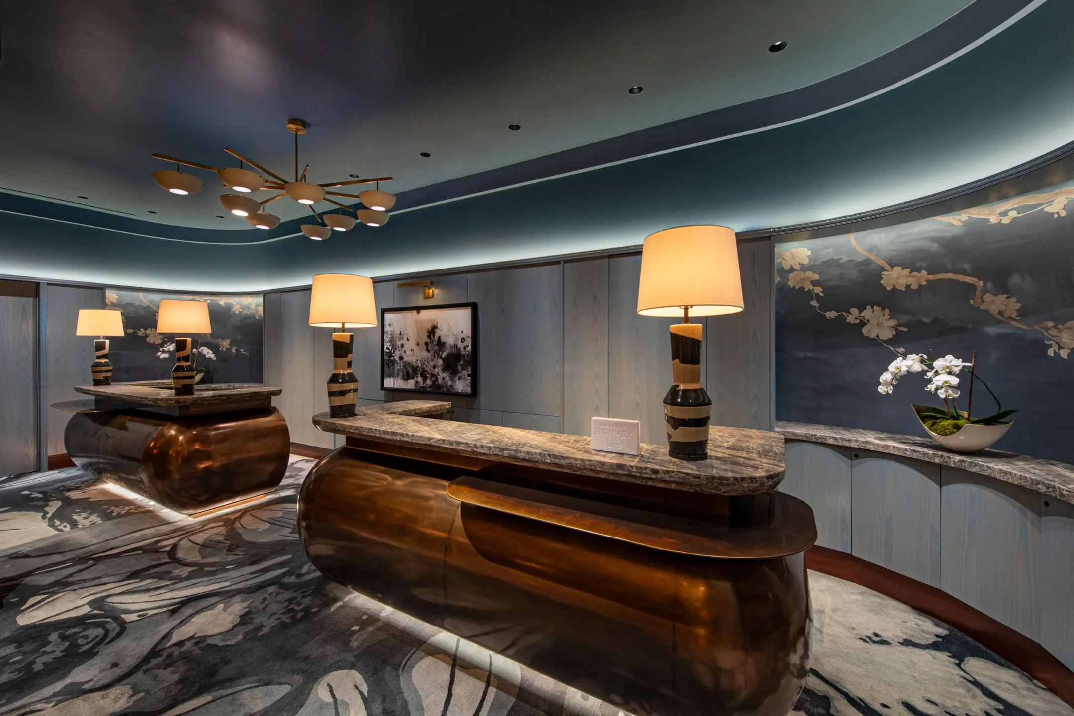 Two concierge desks with marble tops in rounded steel blue room with orchids behind