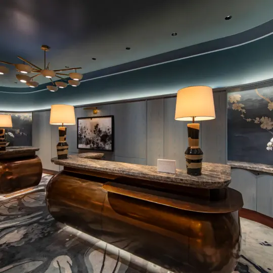 Two concierge desks with marble tops in rounded steel blue room with orchids behind