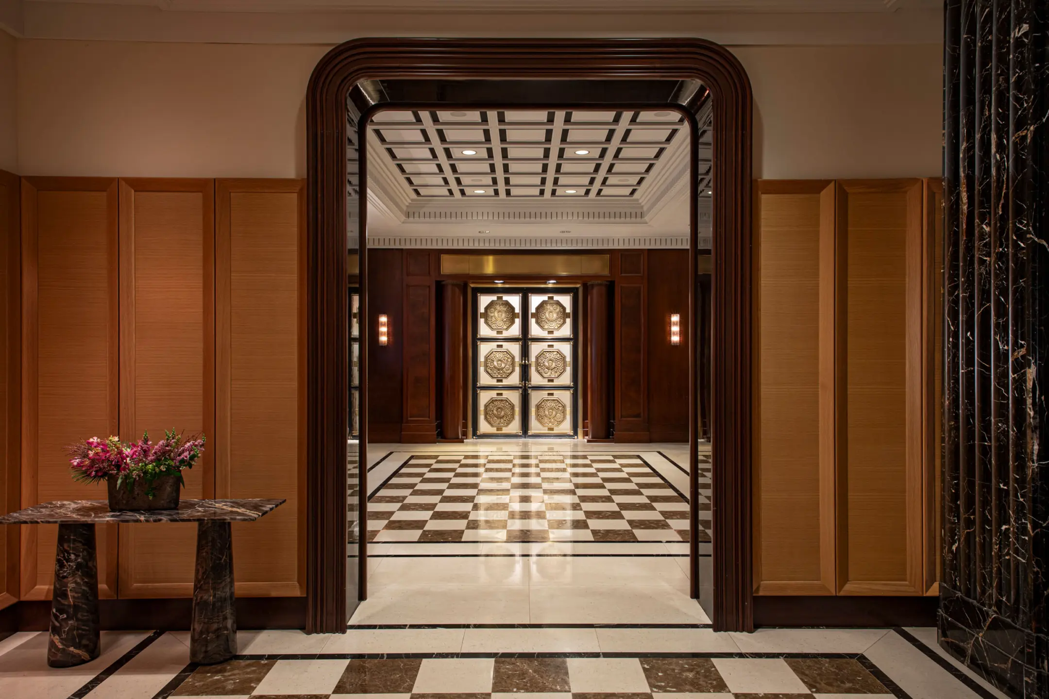 Hallway with checkered marble floor, dark wooden millwork hallway arch, and marble table