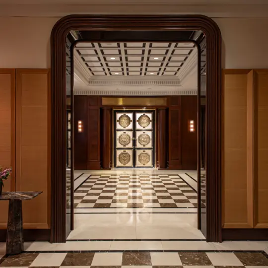 Hallway with checkered marble floor, dark wooden millwork hallway arch, and marble table